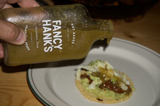 Fancy Hank's Jalapeno and Peach hot sauce being poured over a sticky BBQ chicken taco topped with cabbage slaw and smashed avocado