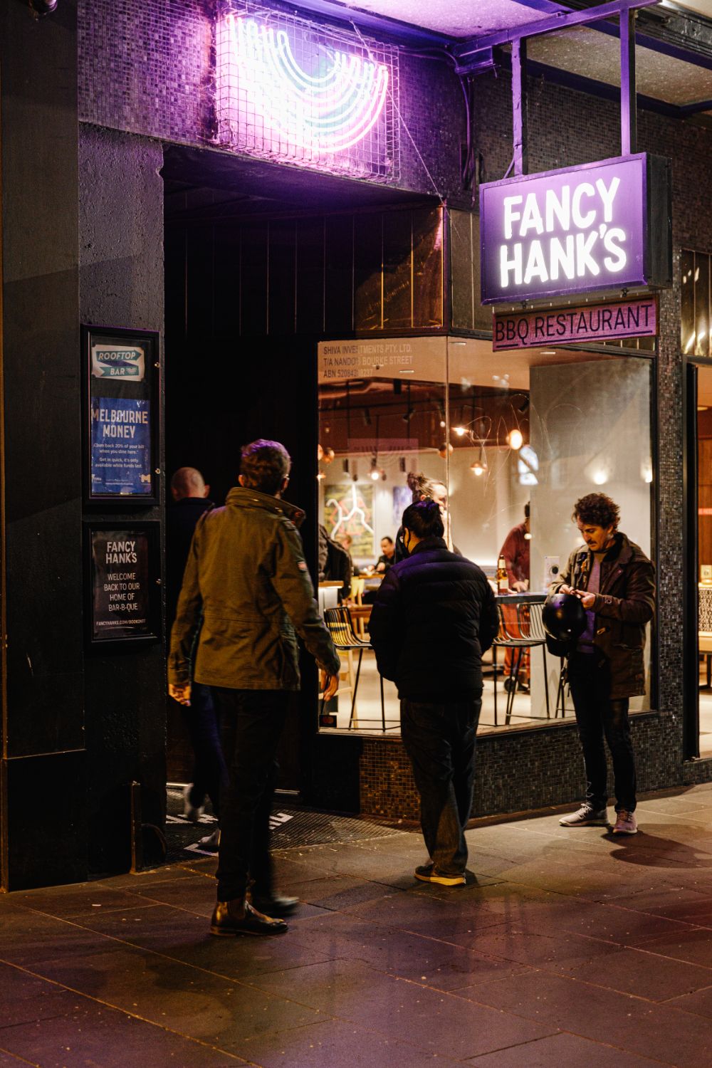 Guests gathered under the lit Fancy Hank's sign on Bourke Street at night
