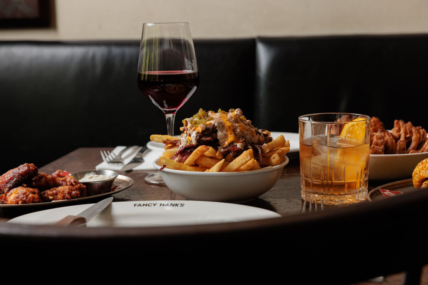 A table spread of BBQ, wings and drinks with a glass of red wine