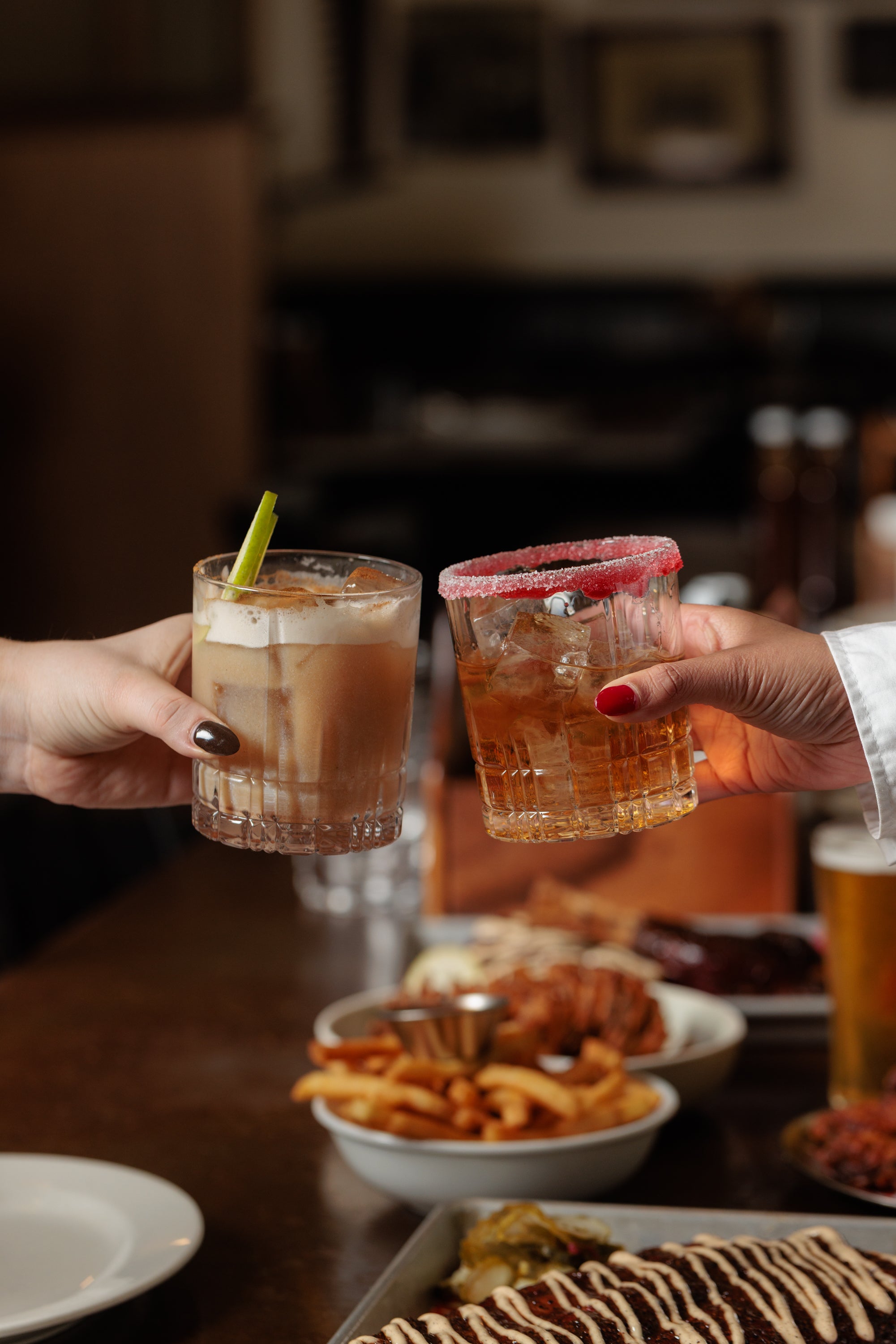 Two hands toasting over a table of shared food
