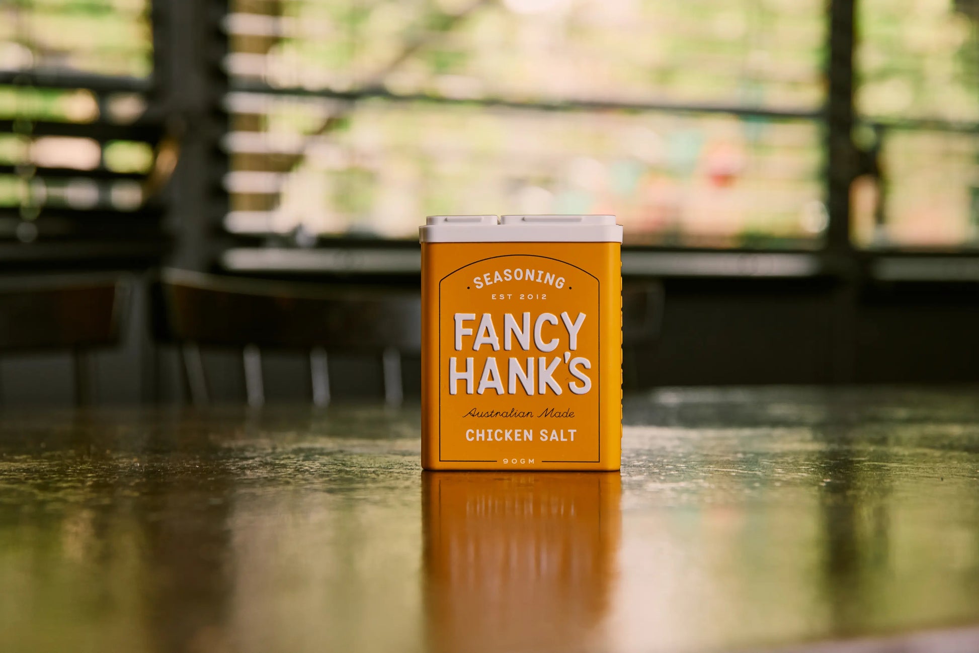 Fancy Hanks seasoning container on a wooden surface with a blurred background